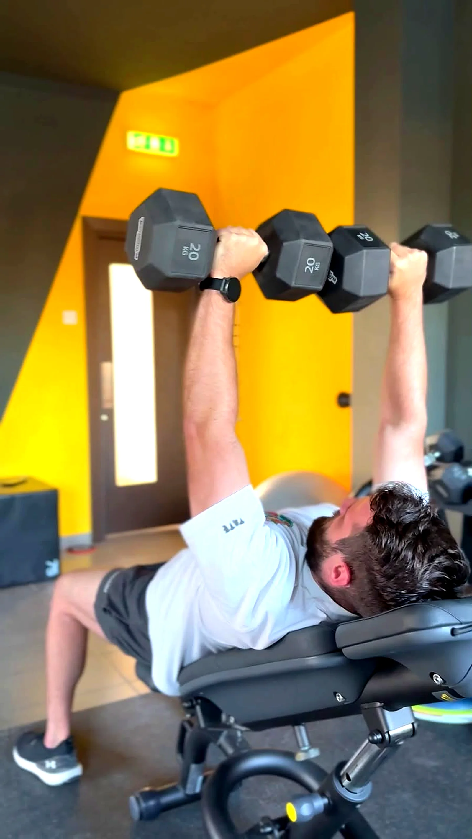 Man doing a dumbbell bench press during personal training in front of the yellow wall in Peyia