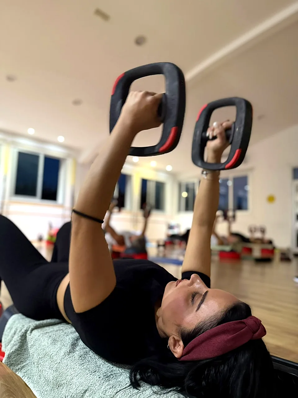 Woman pressing dumbbells on a bench in a strength class at Rewell Emotion Fitness, Peyia