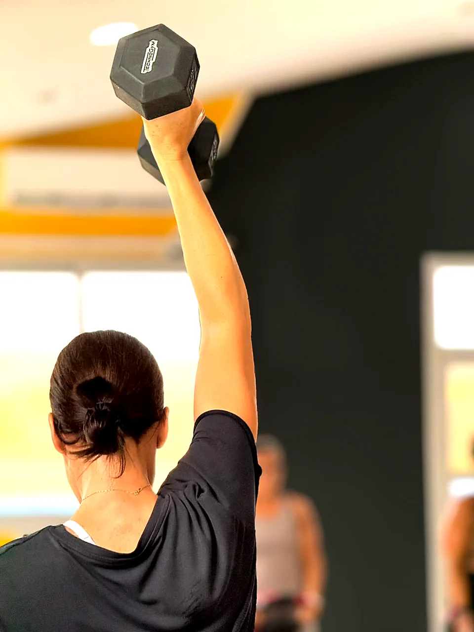 Woman pressing a dumbbell overhead in a Strength & Conditioning class in Peyia
