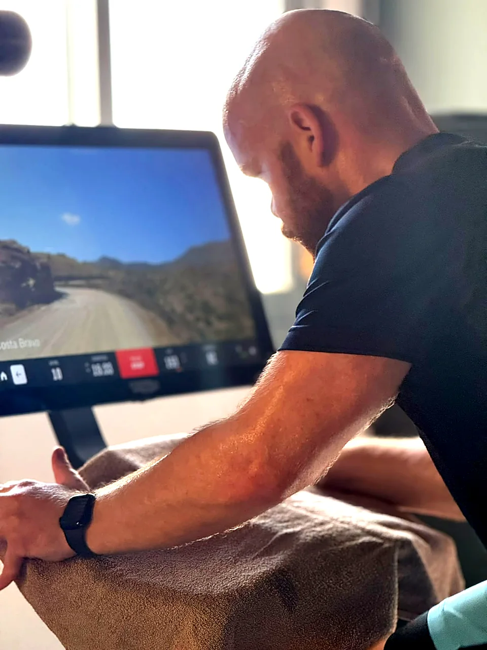 Member riding a Technogym indoor bike with a virtual route on screen in Peyia