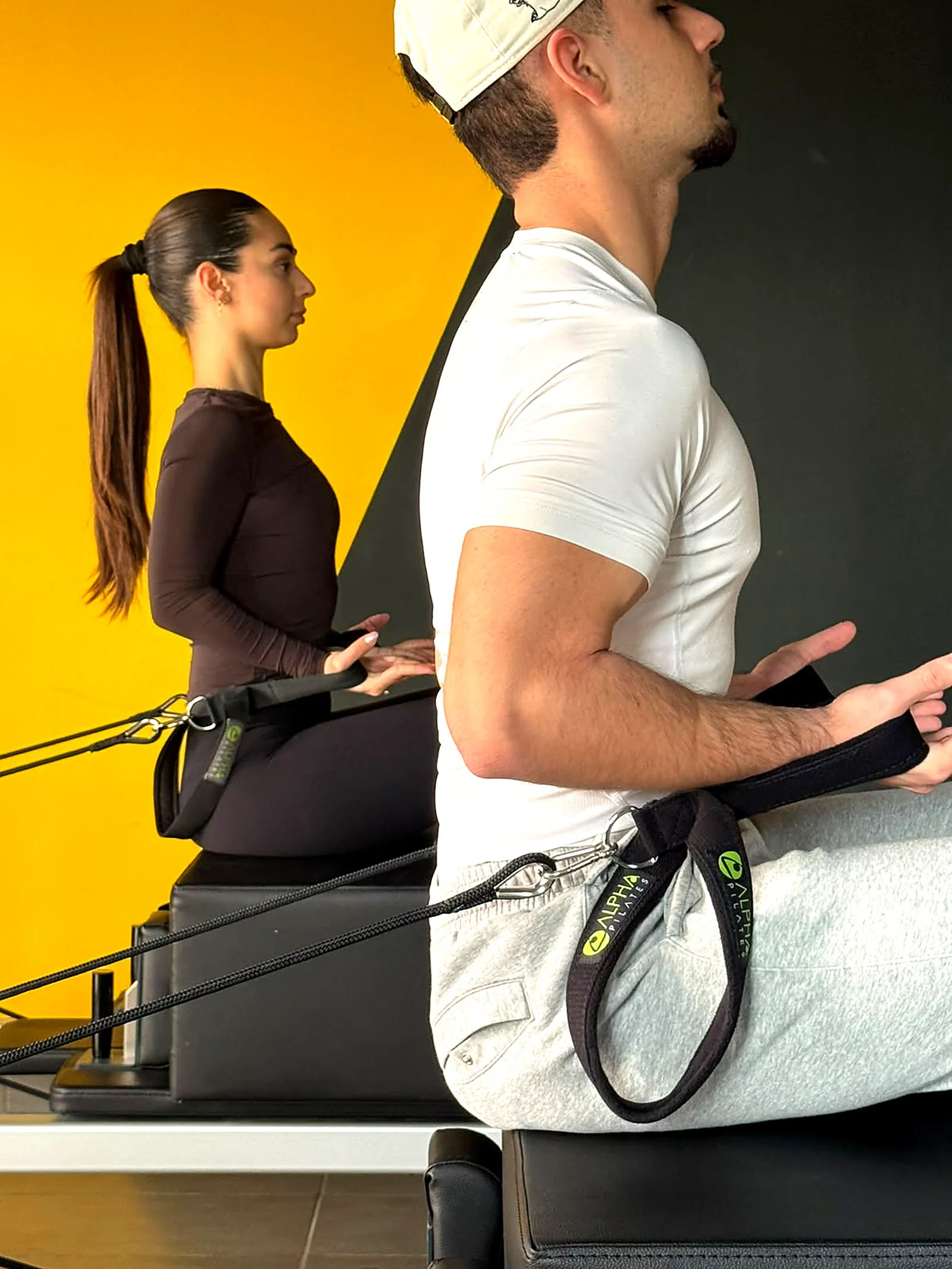 Two clients sitting on the reformer box doing a rowing exercise with straps in Peyia