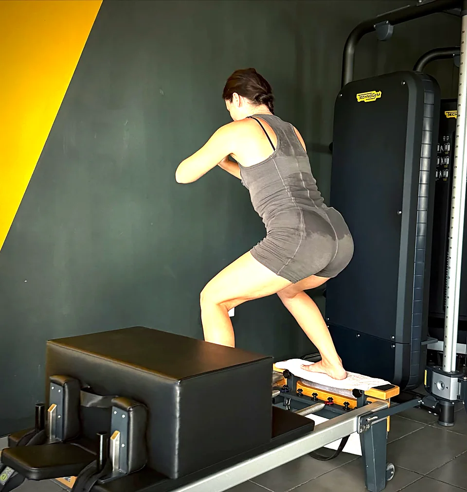 Woman squatting on a Pilates Reformer with jump box in a private session in Peyia