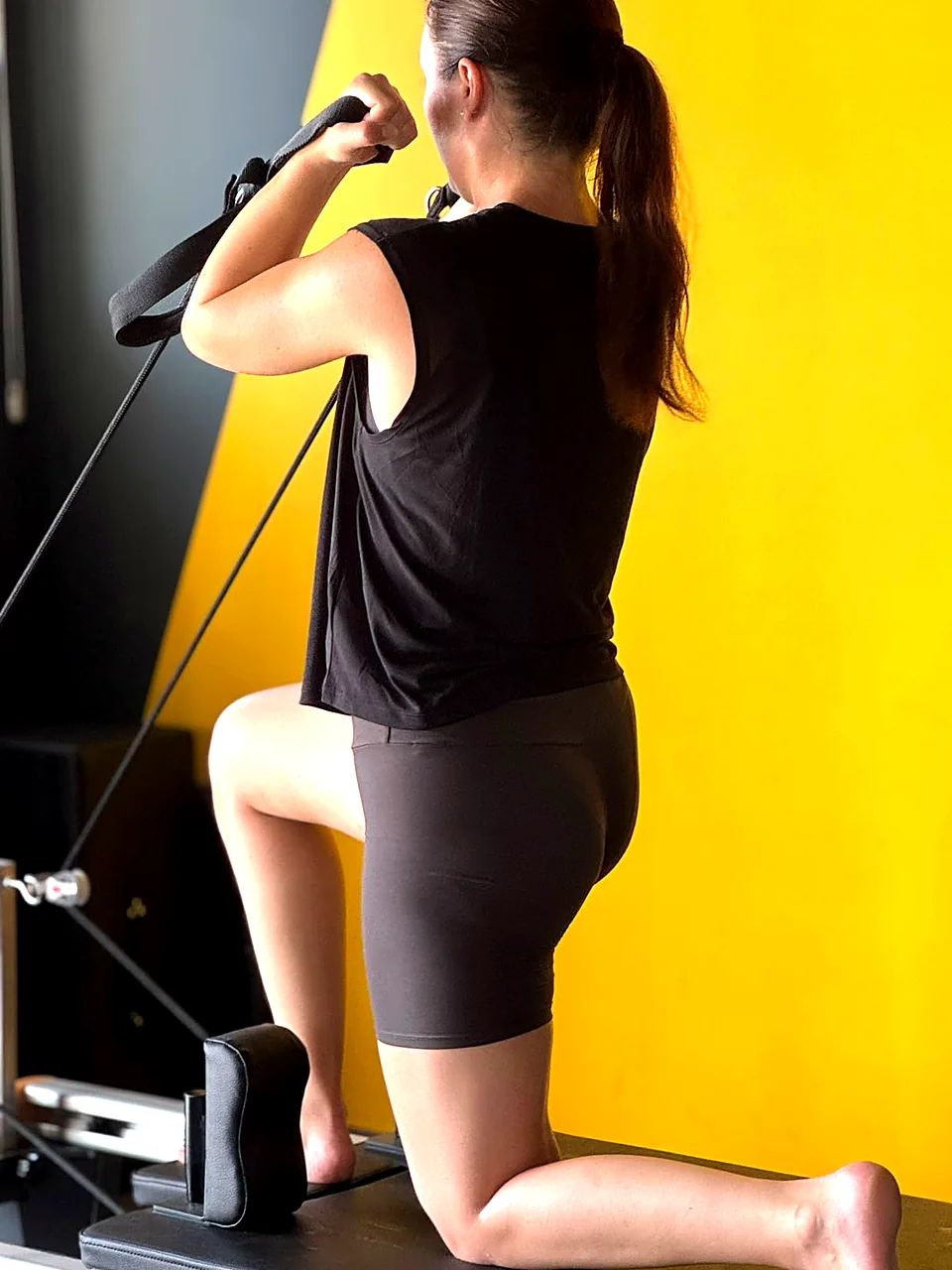 Woman kneeling on a Pilates Reformer doing arm work with straps in Peyia
