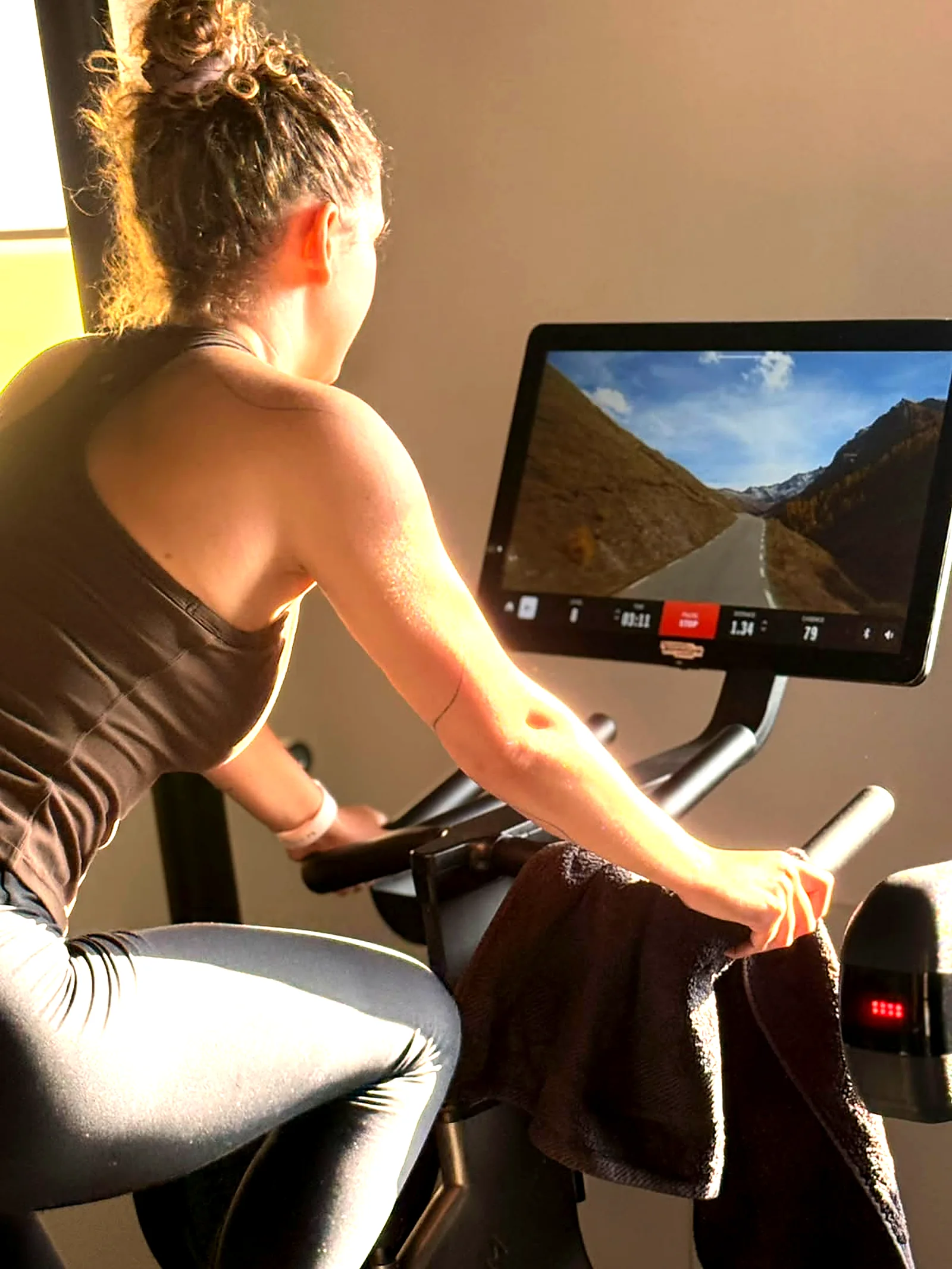 Woman riding a Technogym indoor bike with a virtual mountain route in the gym in Peyia